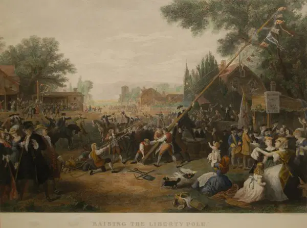 The townsfolk raising a tall wooden colonial flag pole in a historic American town square.