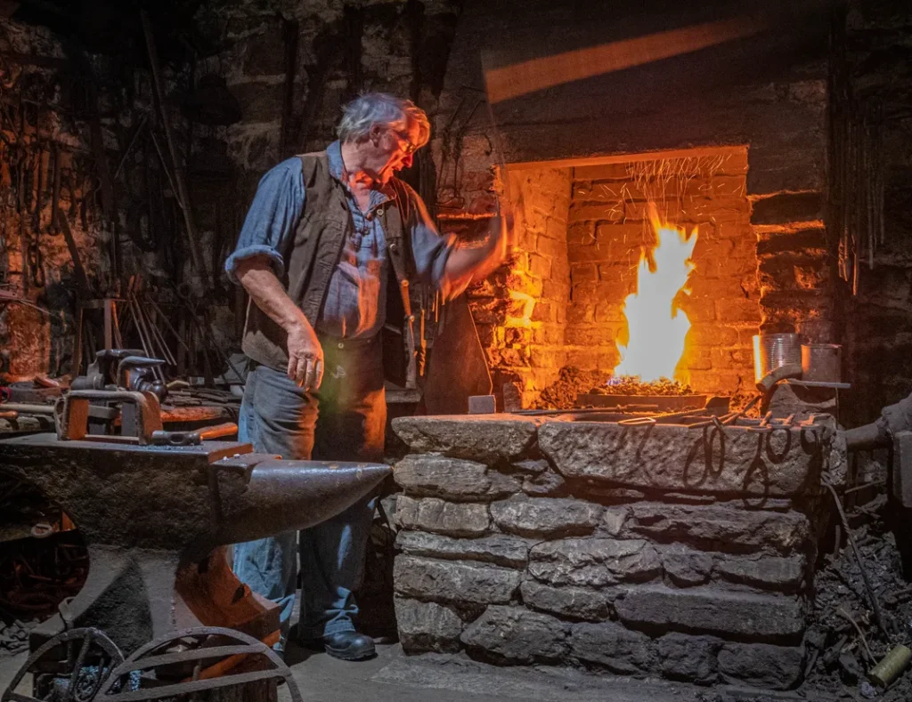 An historic close-up of a colonial blacksmith working at a glowing iron forge, representing early American industry.