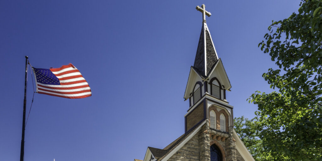 An American flag waving proudly in front of a historic colonial community church.