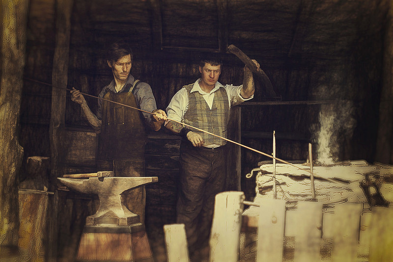 An historic close-up of two colonial blacksmiths working at a glowing iron forge, representing early American industry.